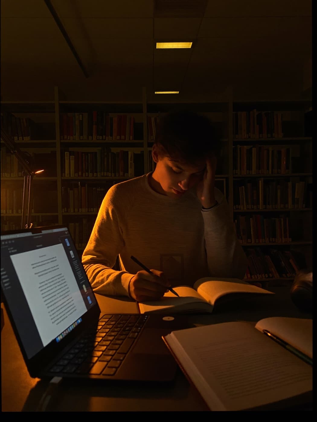 طالب يذاكر ليلاً في مكتبة معتمة تحت ضوء مصباح دافئ